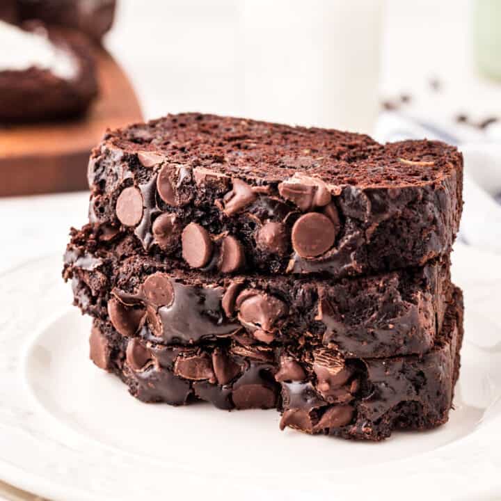 Three slices of chocolate zucchini bread stacked on a white plate.