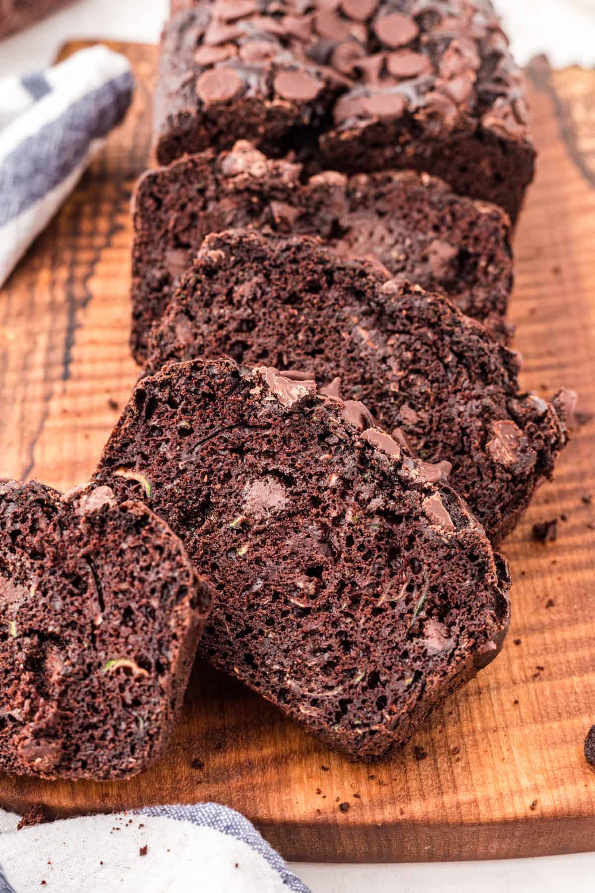 Loaf of chocolate zucchini bread on wooden cutting board cut into slices.