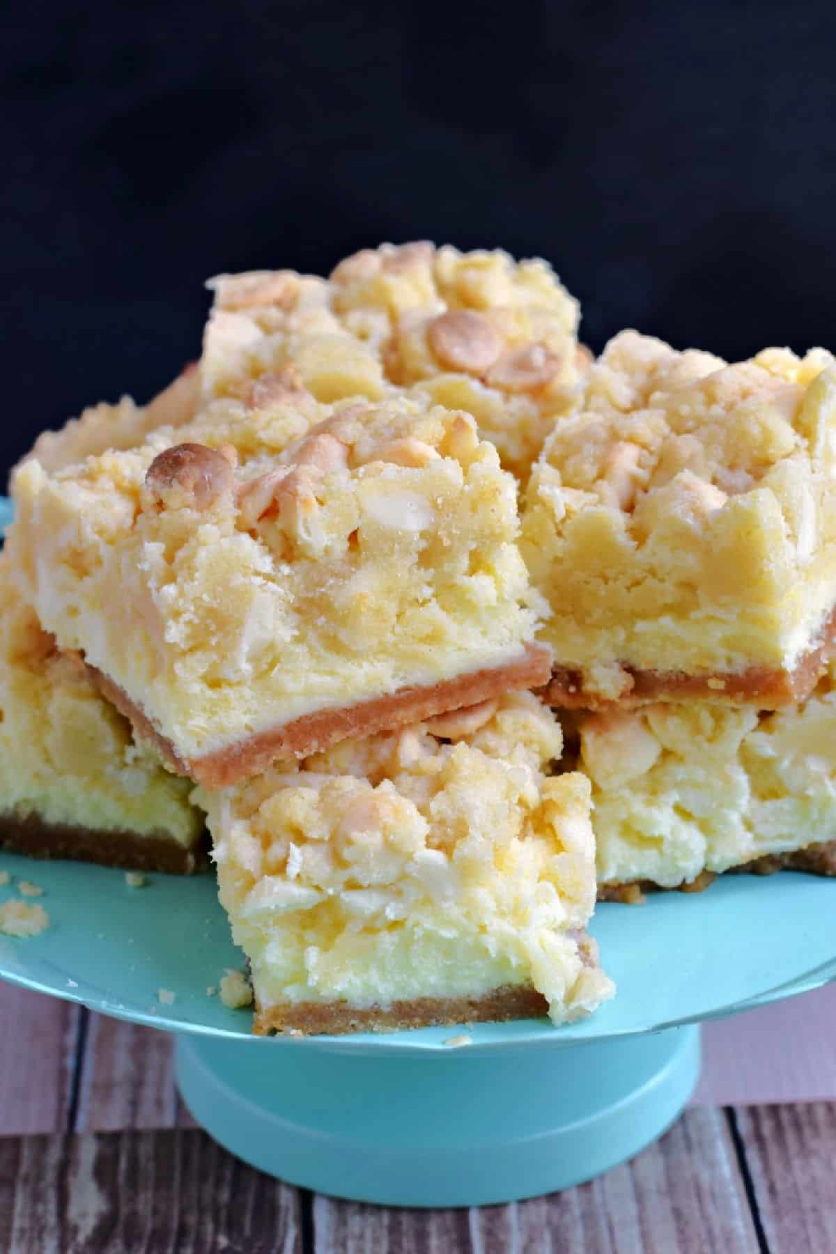 Squares of lemon cheesecake cookie bars on a teal cake platter.