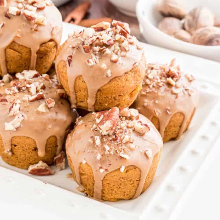 Mini pumpkin muffins with maple glaze stacked on a white platter.