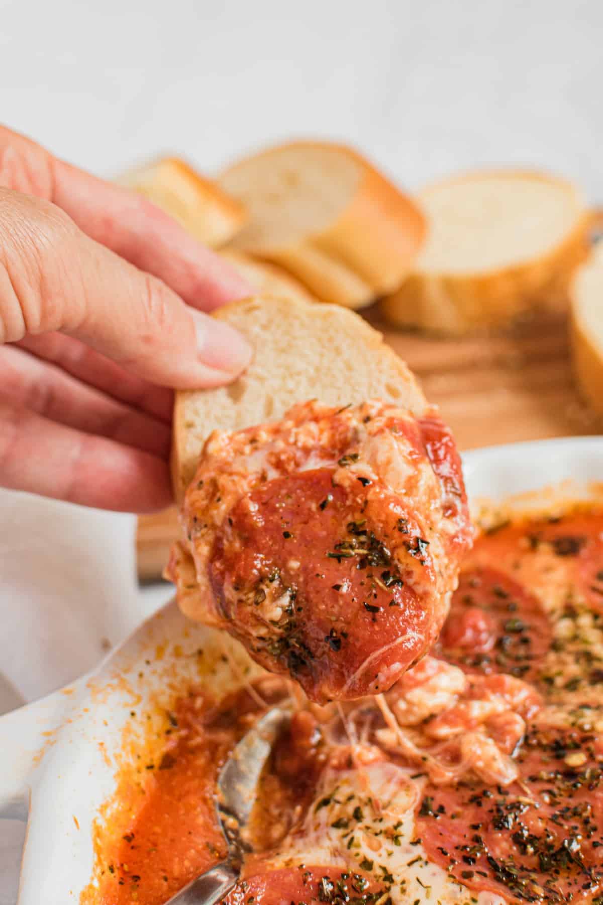 Slice of french bread being dipped in the pepperoni pizza dip.
