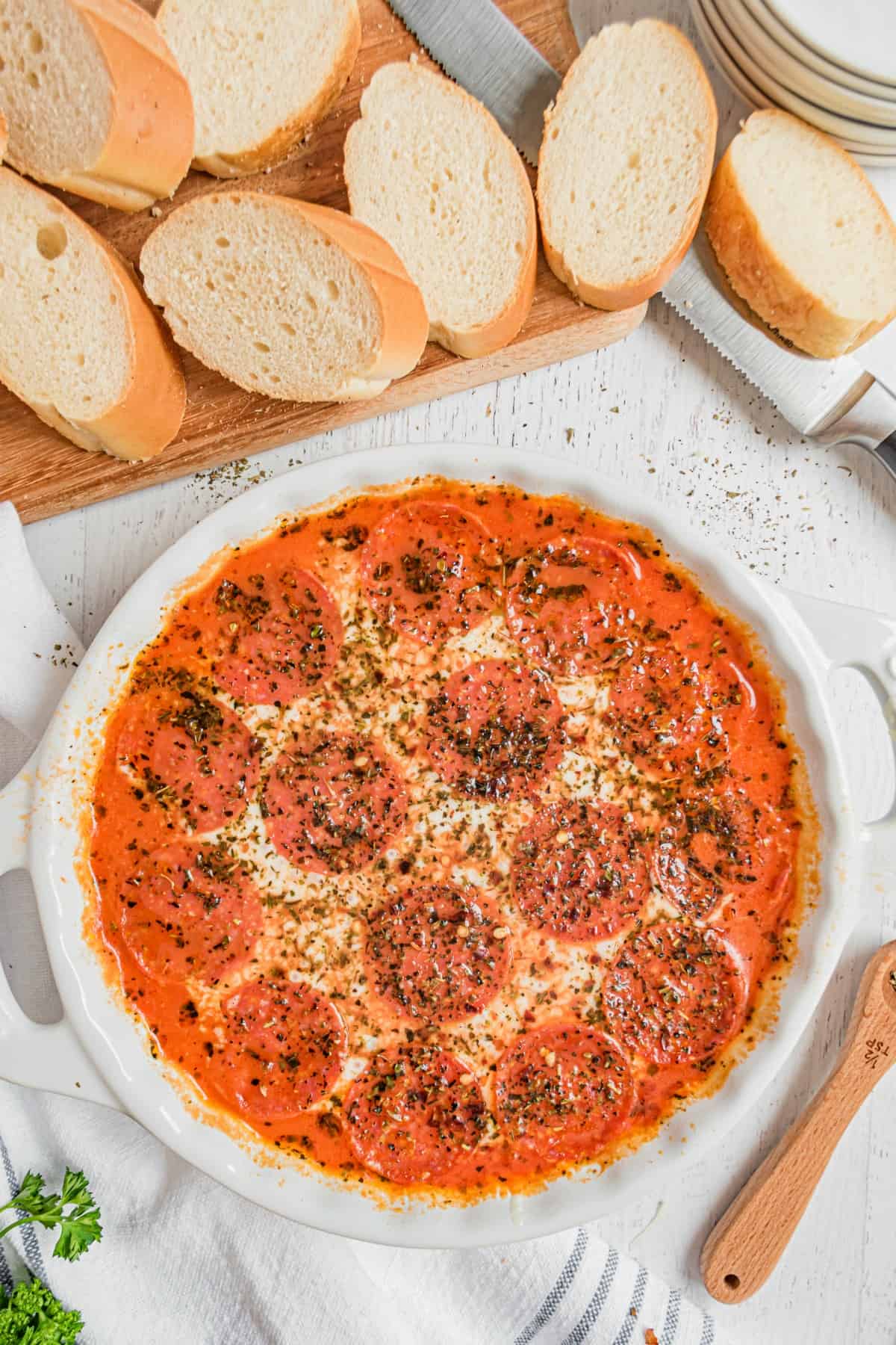 Pepperoni pizza dip in a white pie plate surrounded by sliced french bread for dipping.