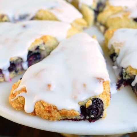 Blueberry scone with lemon icing on a white plate.