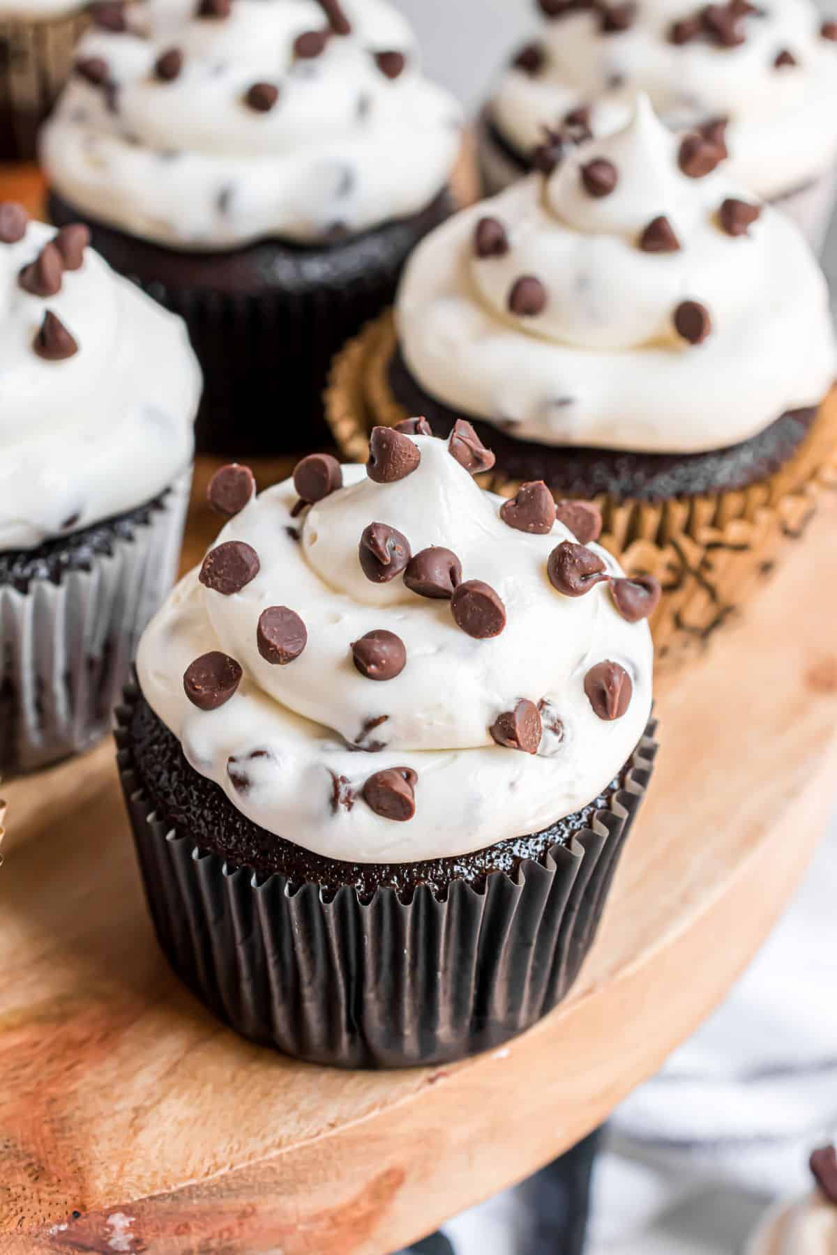 Chocolate chip cheesecake frosted chocolate cupcakes on a wooden serving platter.