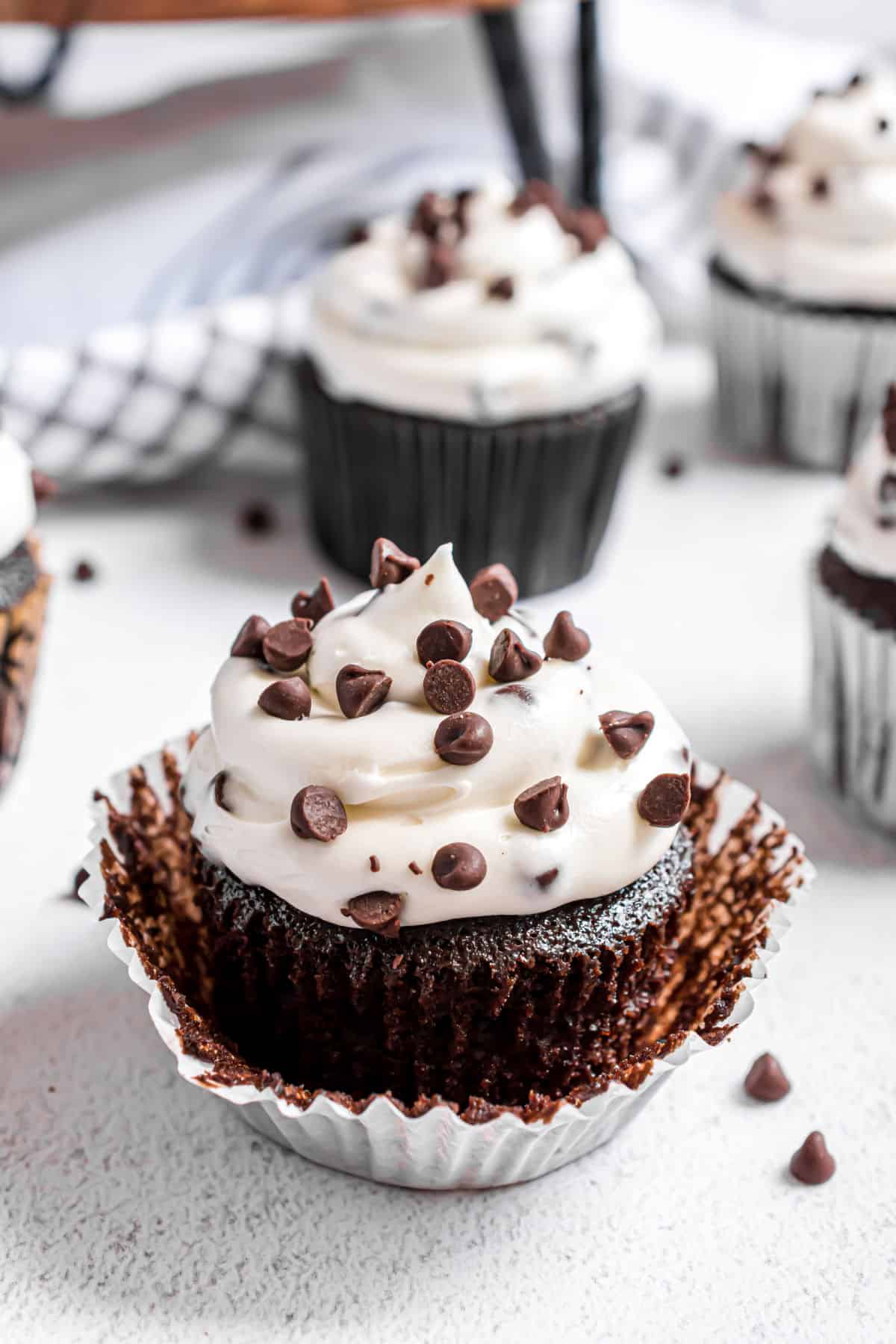 Chocolate cupcake unwrapped and topped with cream cheese frosting and mini chocolate chips.