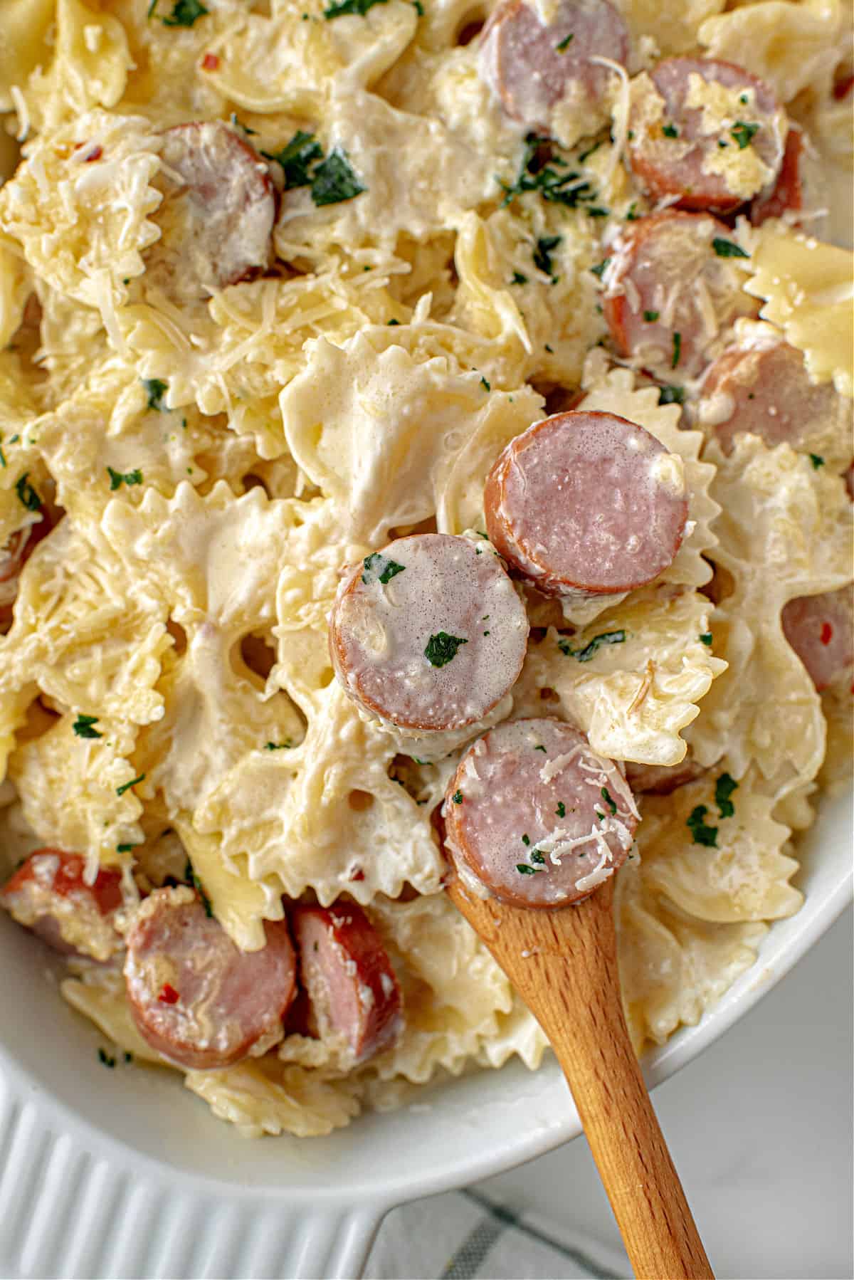 Bowtie pasta with sausage slices and alfredo sauce in a baking dish.