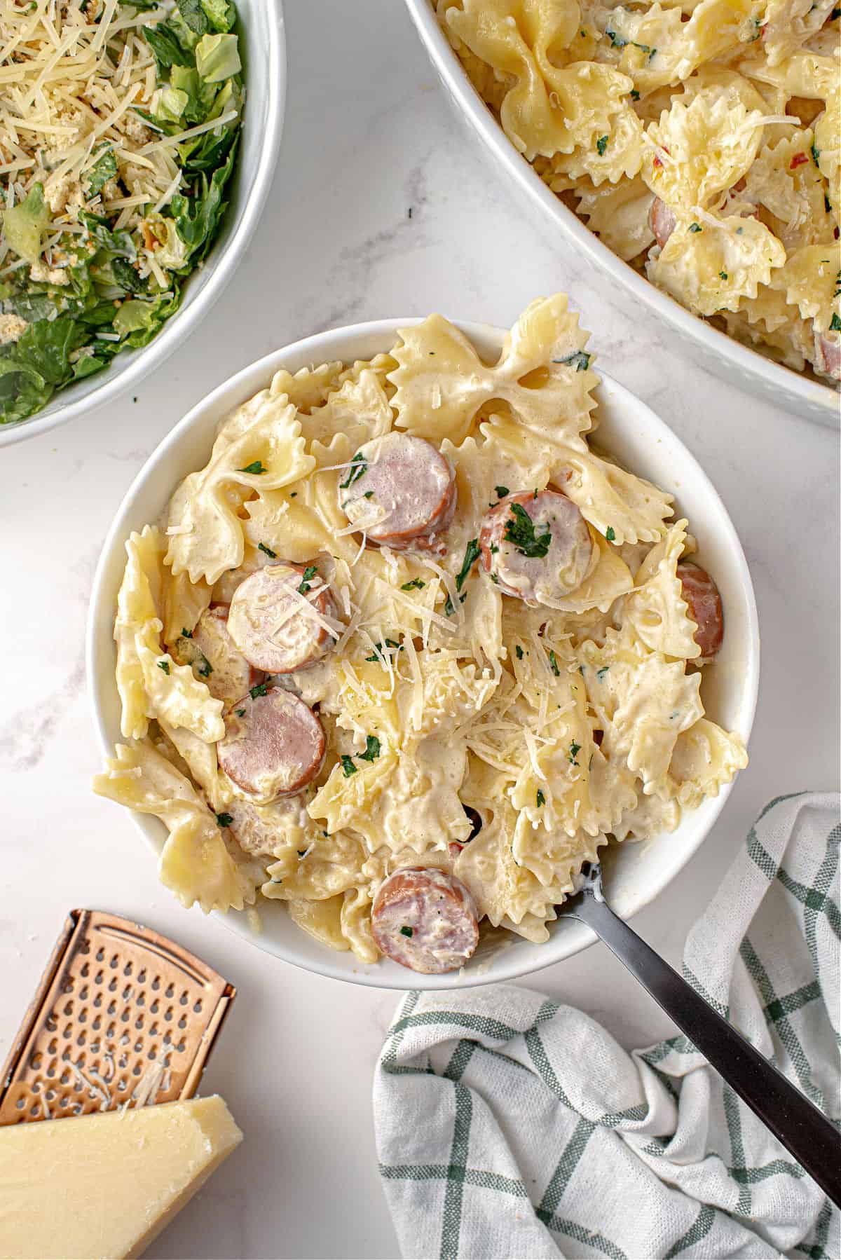 Alfredo pasta with sausage served in a white bowl.