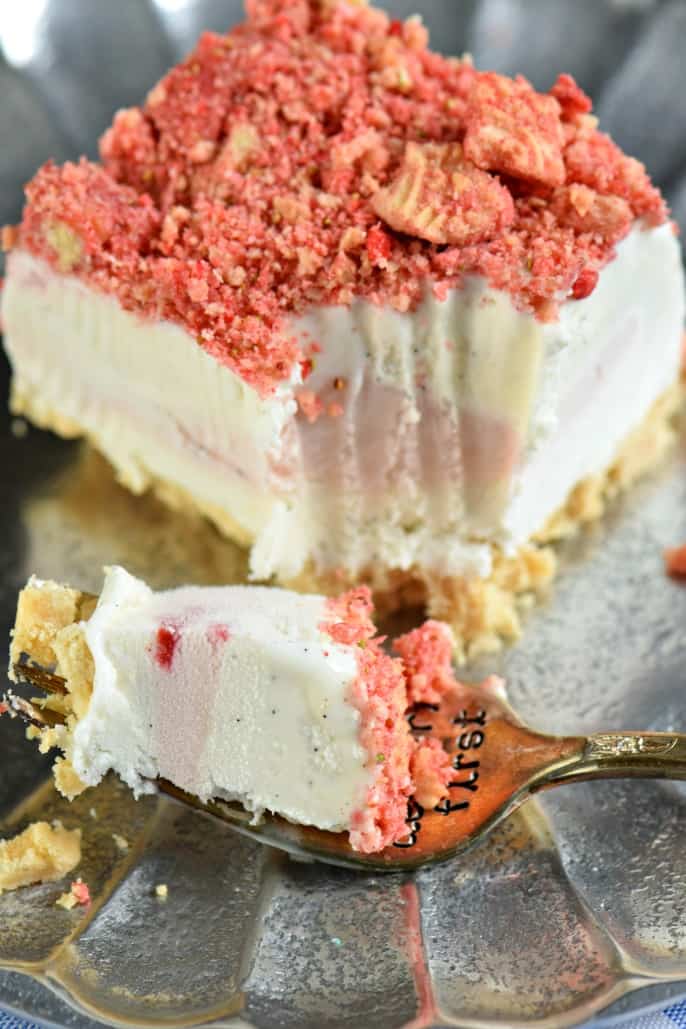 Fork full of strawberry shortcake ice cream with a slice of cake in background.