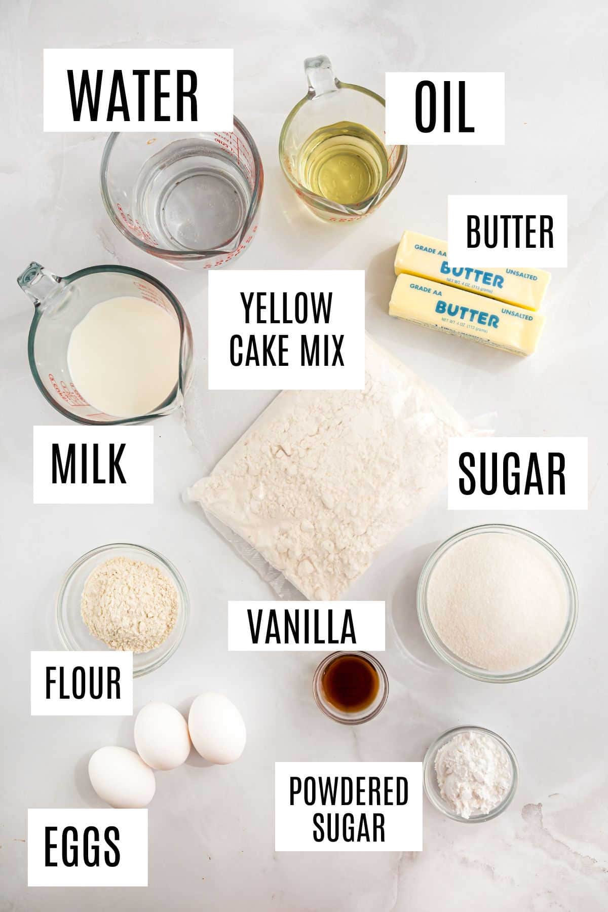 Overhead view of labeled baking ingredients for a delicious twinkie cake recipe: water, oil, butter, cake mix, milk, sugar, flour, eggs, vanilla, powdered sugar.