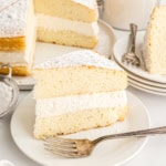 A slice of sponge cake with cream filling and powdered sugar on a white plate with a fork, inspired by a classic twinkie cake recipe.