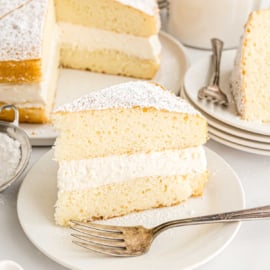 A slice of sponge cake with cream filling and powdered sugar on a white plate with a fork, inspired by a classic twinkie cake recipe.