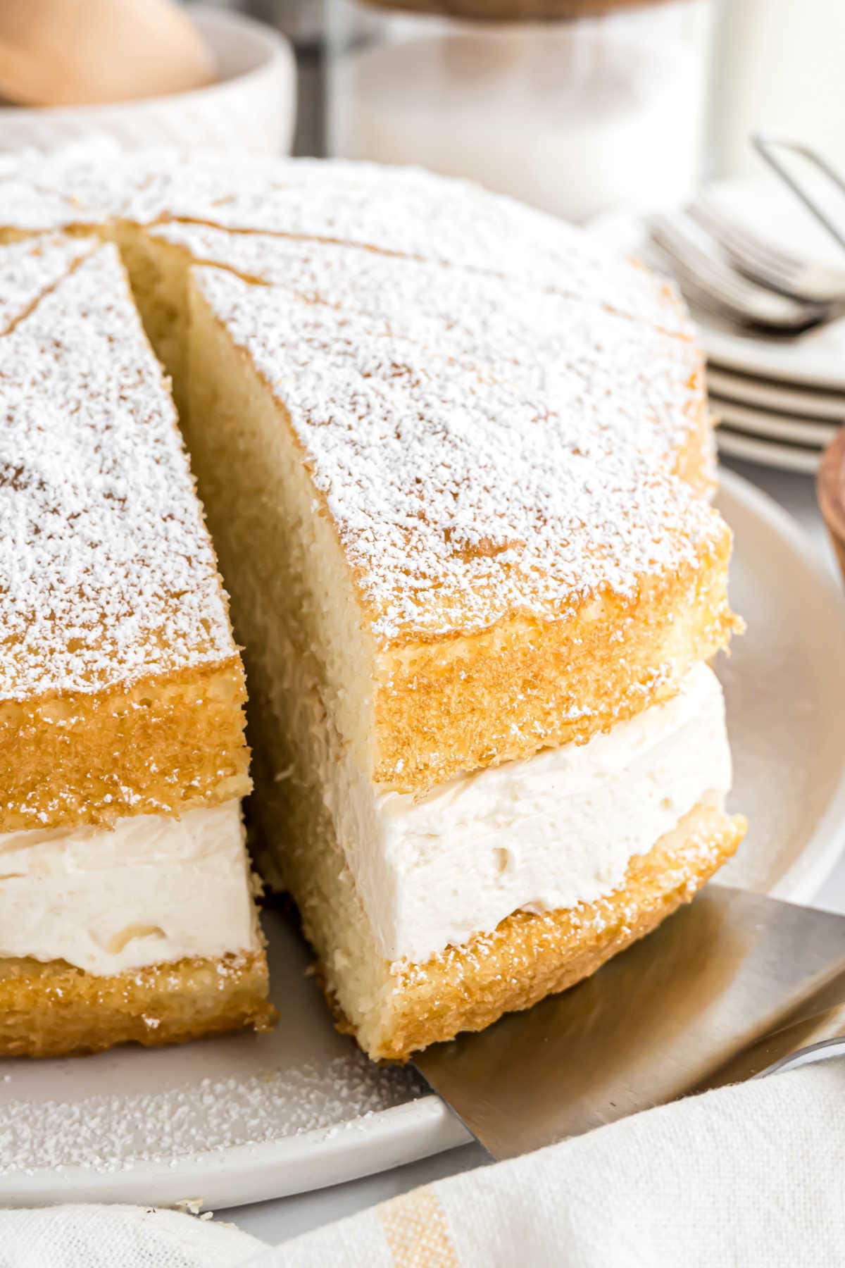 A slice of sponge cake with powdered sugar and cream filling is being lifted from a plate, reminiscent of a classic Twinkie cake recipe.