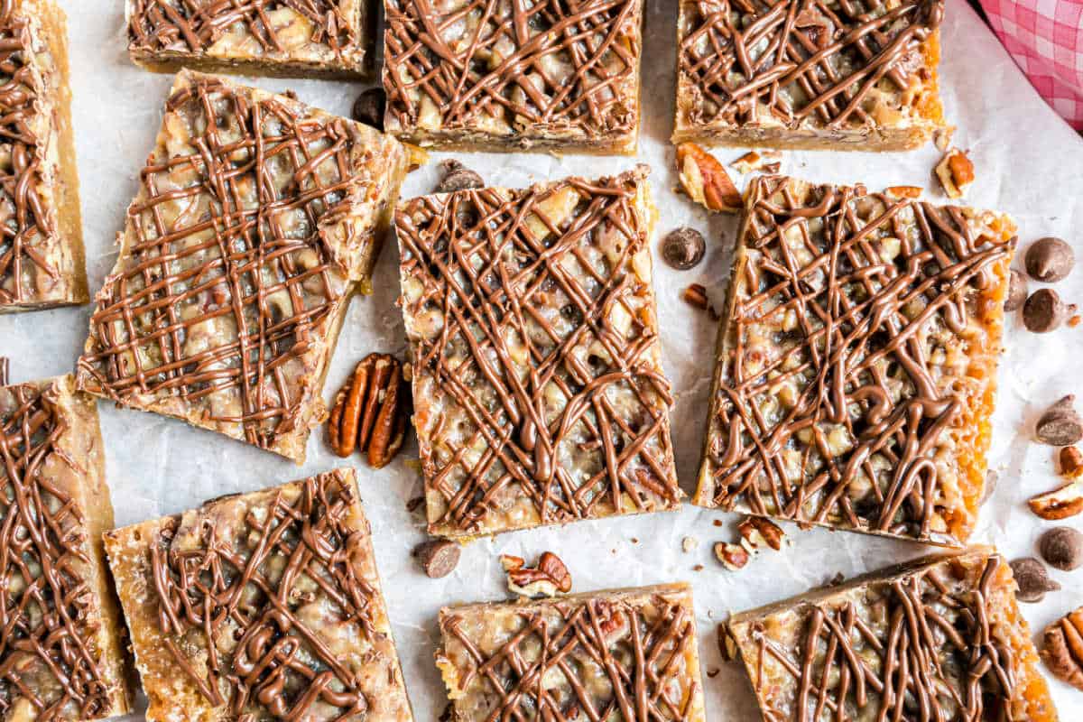 Rectangular pecan pie blondies with chocolate drizzle and pecans rest on parchment paper.
