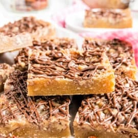 Stack of pecan pie blondies with a nutty base and chocolate drizzle on top, placed on a countertop.