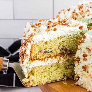 Watergate Cake brings together pistachio, coconut, and pudding in a delicious layer cake! A light whipped frosting and pecans on top make it hard to stop at just one slice.
