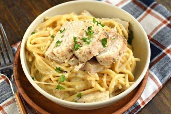 Bowl of creamy chicken alfredo on a plaid napkin with fork