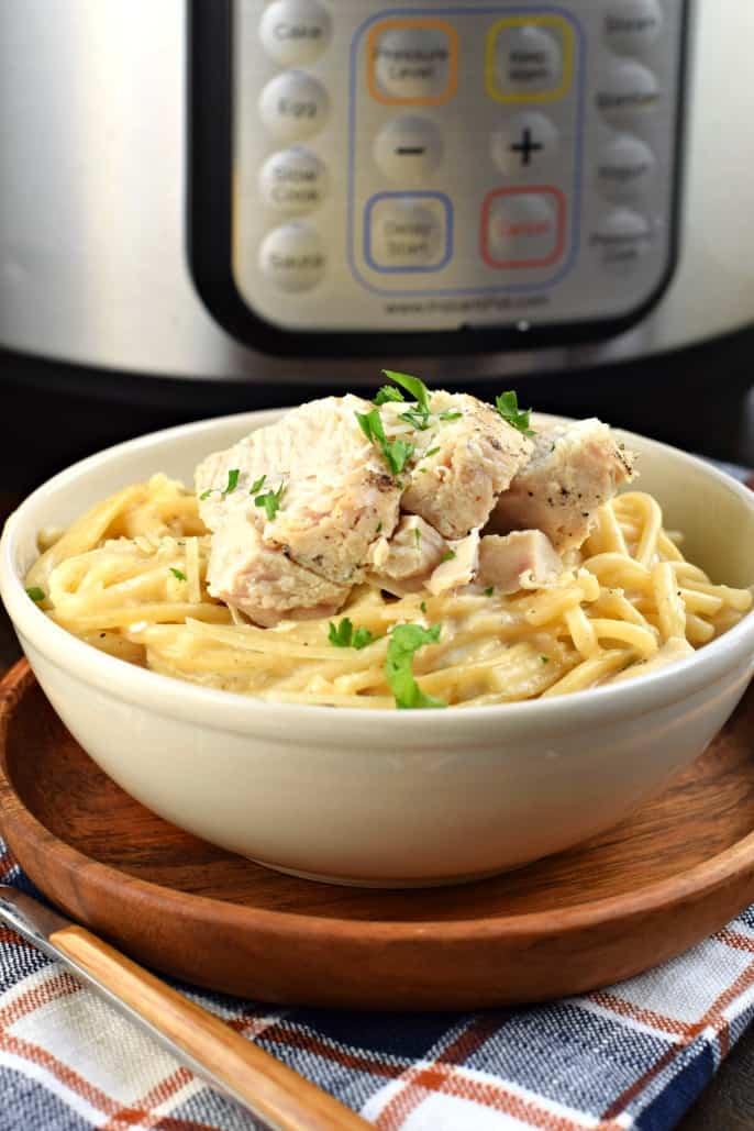 Instant Pot with bowl of creamy Chicken Alfredo and parsley garnish