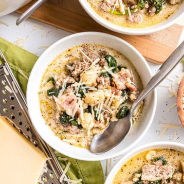 A bowl of creamy low carb keto zuppa toscana with sausage, spinach, cauliflower, and shredded cheese, served with a spoon in the bowl.