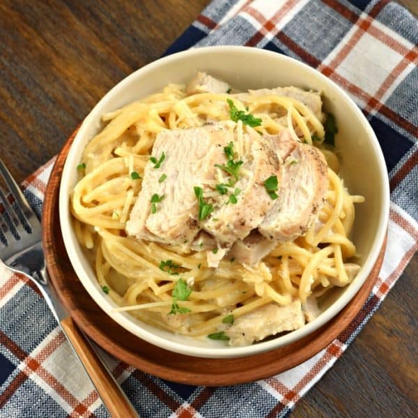 Bowl of fettuccine alfredo topped with chicken and parsley. Served on a plaid napkin and a fork