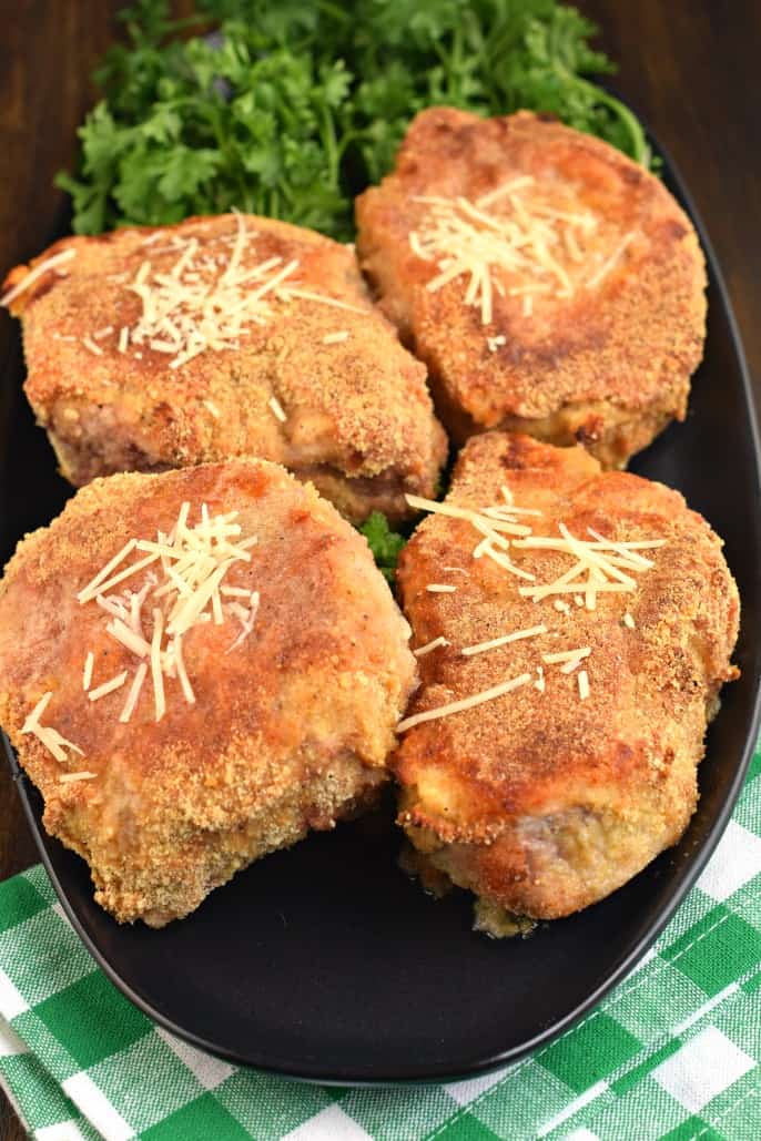 Baked pork chops with parmesan cheese on a black serving plate.