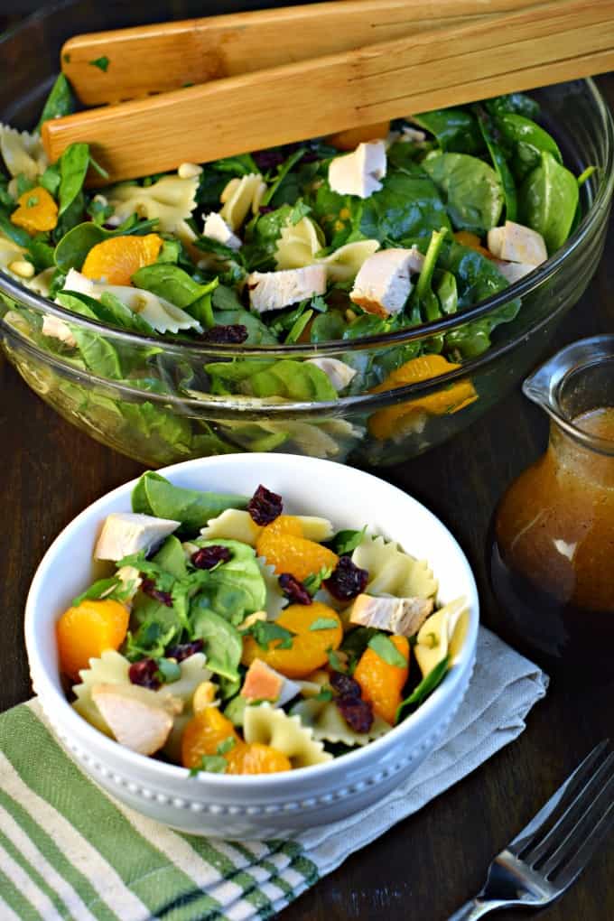 Clear glass salad bowl with wooden tongs and a scoop of salad served into a small white bowl.