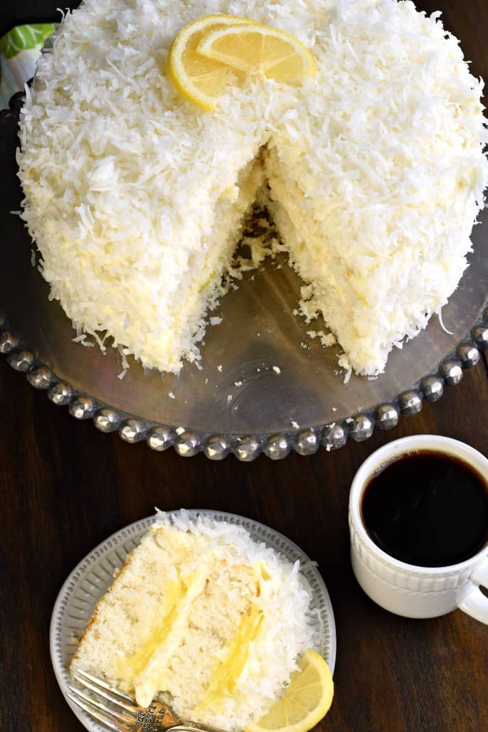 Lemon coconut cake on a silver platter with a slice served on a plate.