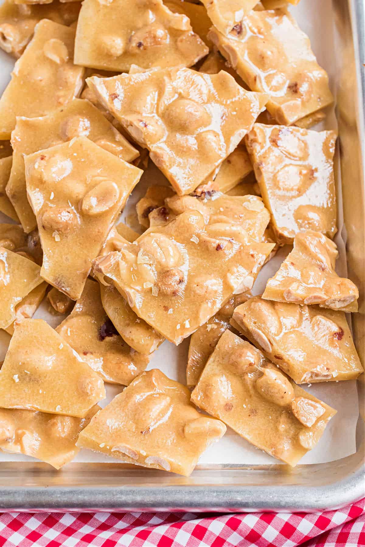 Peanut brittle broken into pieces on a parchment paper lined cookie sheet.