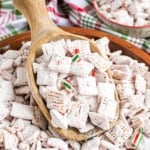 A wooden spoon scoops peppermint puppy chow—powdered sugar-coated cereal and festive holiday candies—from a large bowl.
