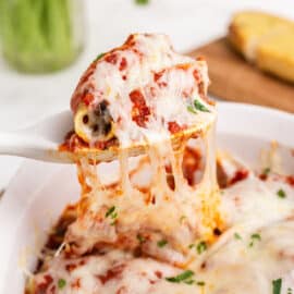 Cheesy sausage stuffed shells being spooned out of baking dish.