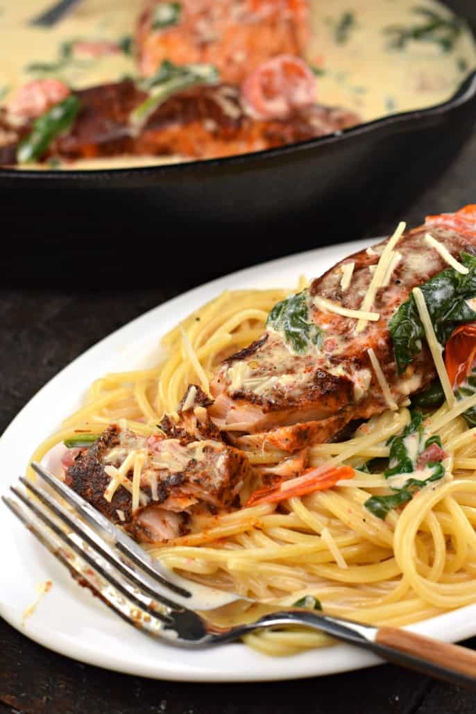 Salmon on a bed of pasta served on a white dinner plate.