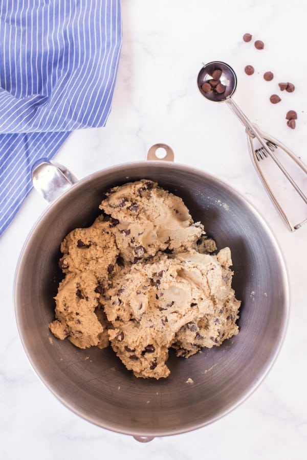 Chocolate chip cookie dough in a mixing bowl with a metal scoop.