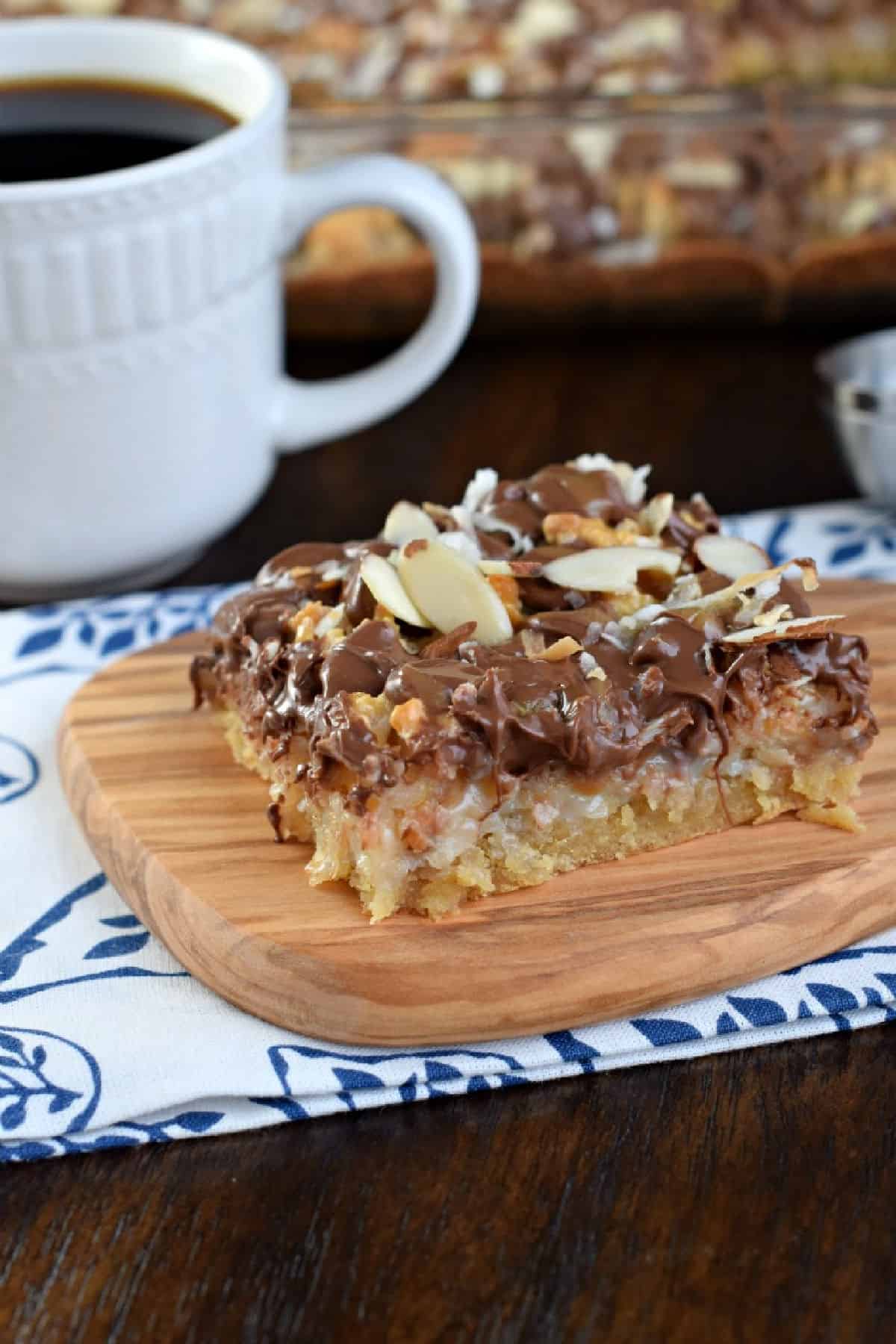 Slice of coconut almond bar on wooden plate with cup of coffee.