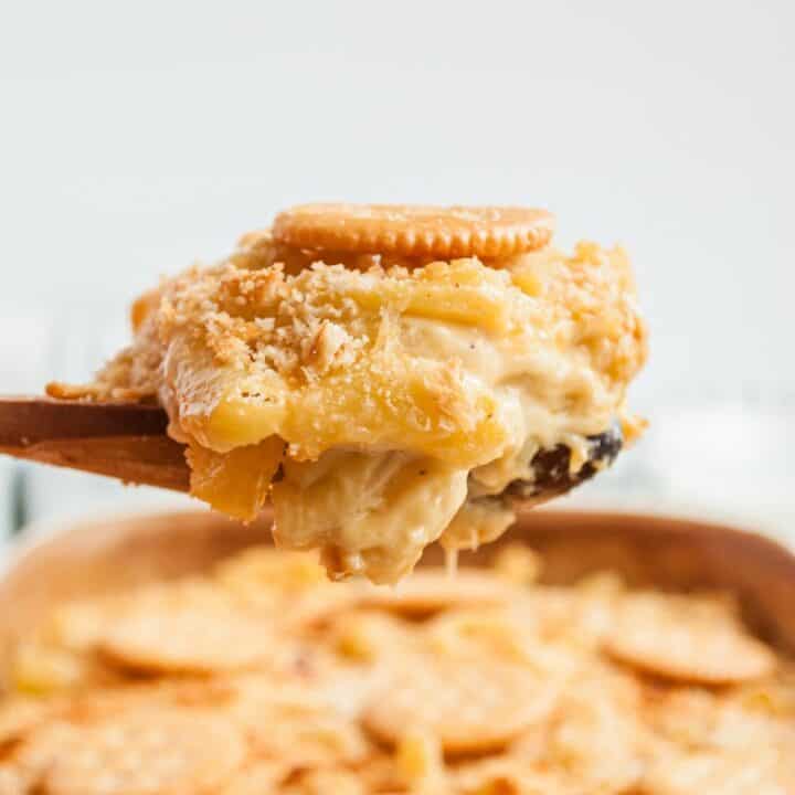 Large scoop dripping with cheese being lifted out of a pan of homemade mac and cheese.
