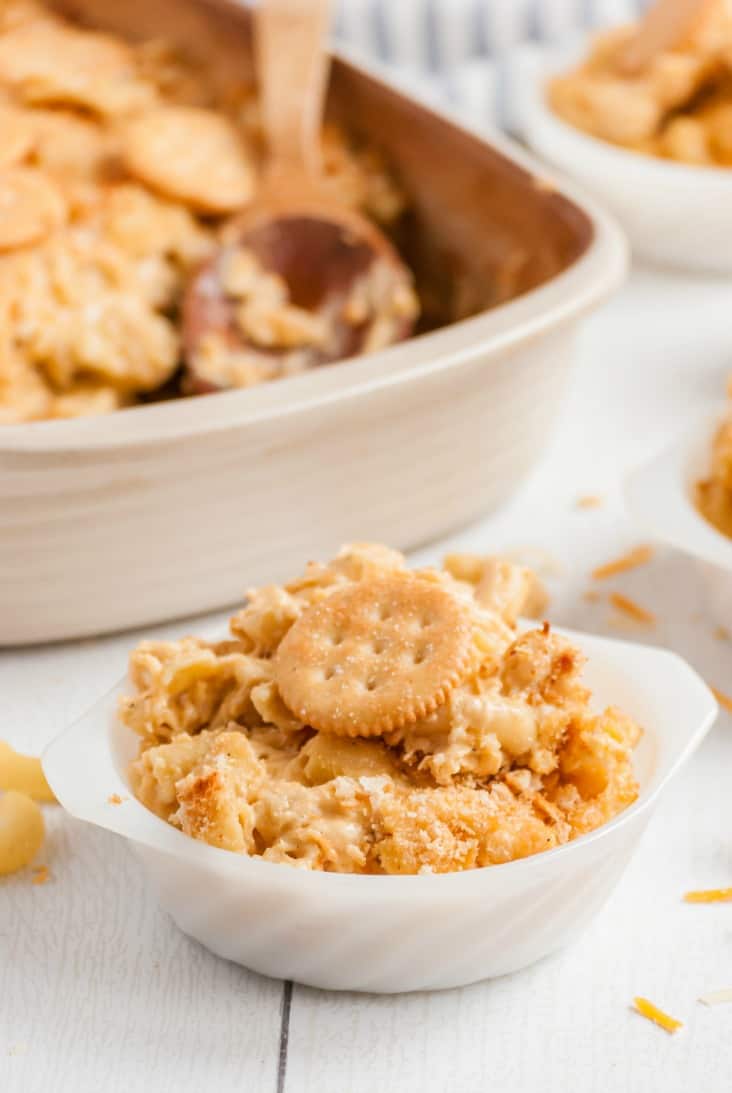 Scoop of homemade mac and cheese topped with a ritz cracker in a white bowl.