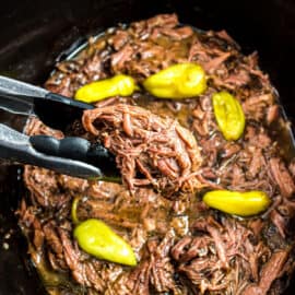 Mississippi pot roast in crockpot being scooped with tongs.