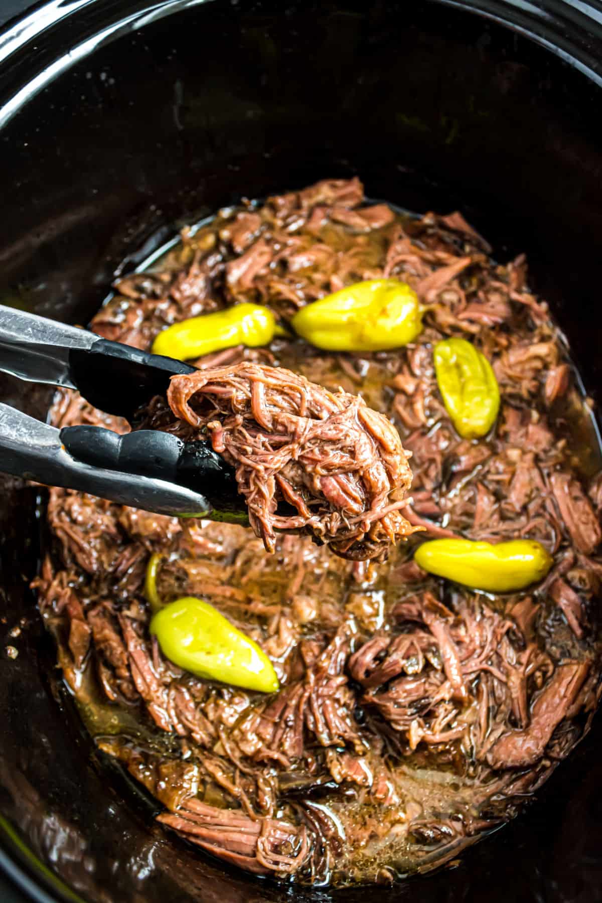 Mississippi pot roast in crockpot being scooped with tongs.