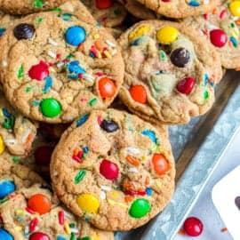 M&M cookies piled on a cookie sheet to serve.