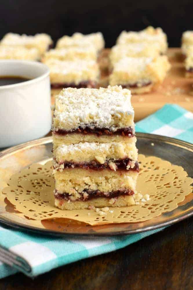 Stack of three Raspberry Shortbread Crumb bars on a silver plate with a white coffee cup.