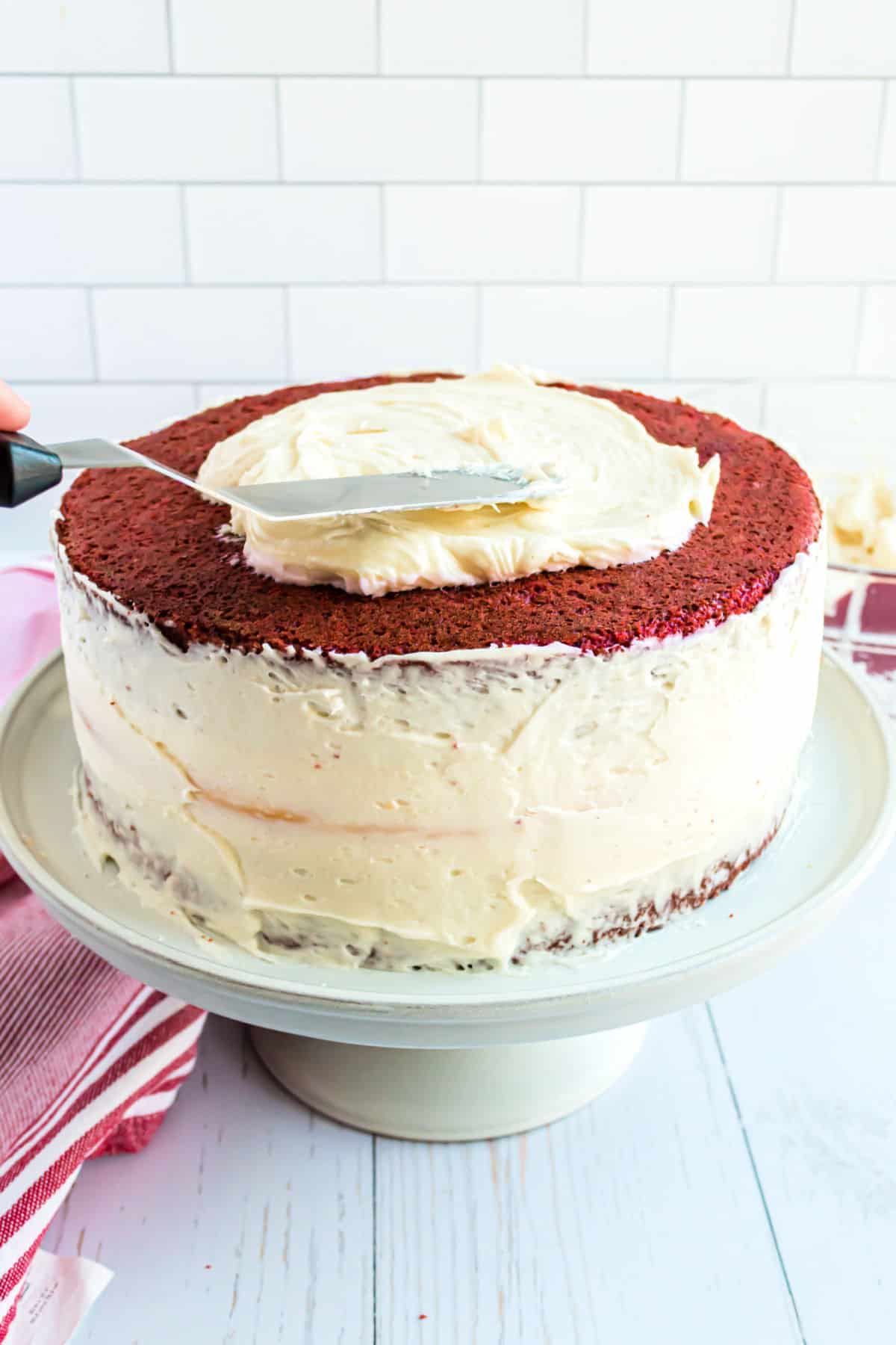 Cream cheese frosting being spread on a red velvet layer cake.