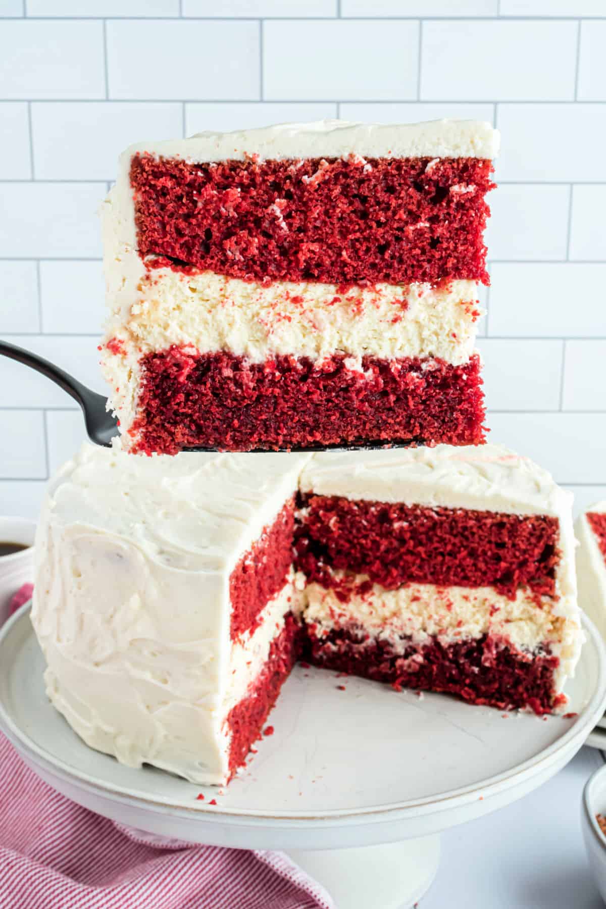 Slice of red velvet cake being lifted off cake plate.