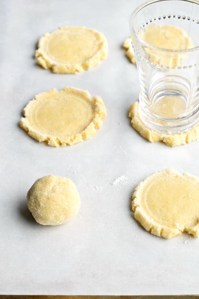 Sugar cookie dough on parchment paper with small glass to press dough balls down.