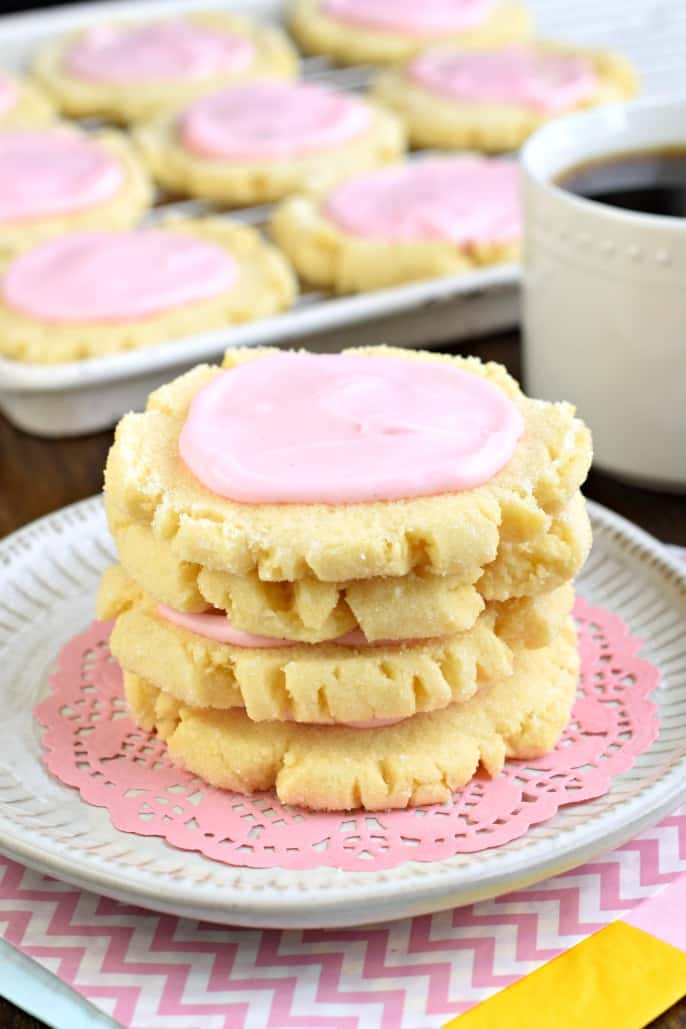 Stack of four sugar cookies with pink frosting on a white plate with pink doily.
