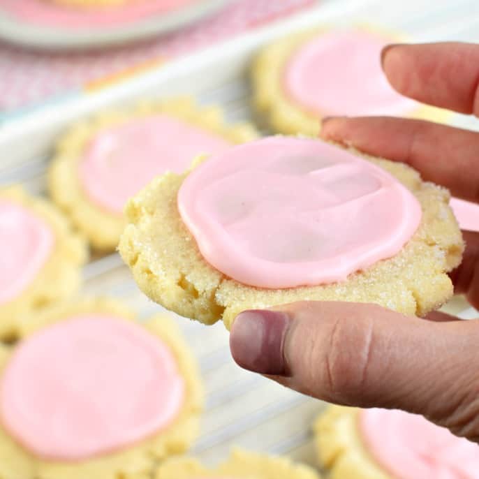 Sugar cookie with pink icing being held up.