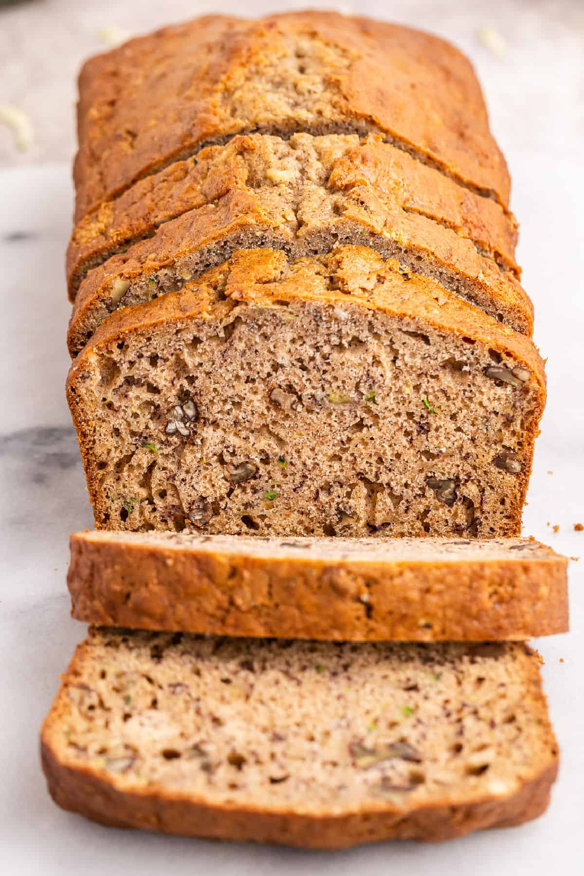 Sliced loaf of zucchini banana bread on cutting board.