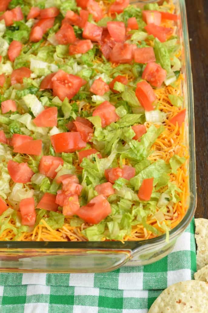 The Ultimate 7 Layer Dip recipe is packed with layers of Cream Cheese, Sour Cream, Ground Beef (and/or Beans), Guacamole, Salsa, Cheese, and more! 7 Layer dip topped with lettuce and tomato.