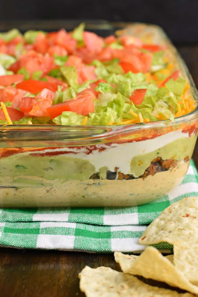 Seven layer dip in a glass bowl served with tortilla chips.