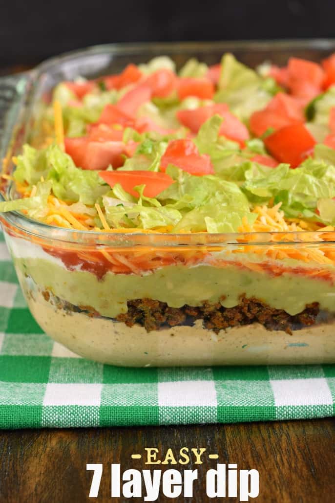 The Ultimate 7 Layer Dip recipe is packed with layers of Cream Cheese, Sour Cream, Ground Beef (and/or Beans), Guacamole, Salsa, Cheese, and more! 7 Layer dip in a clear glass serving dish.
