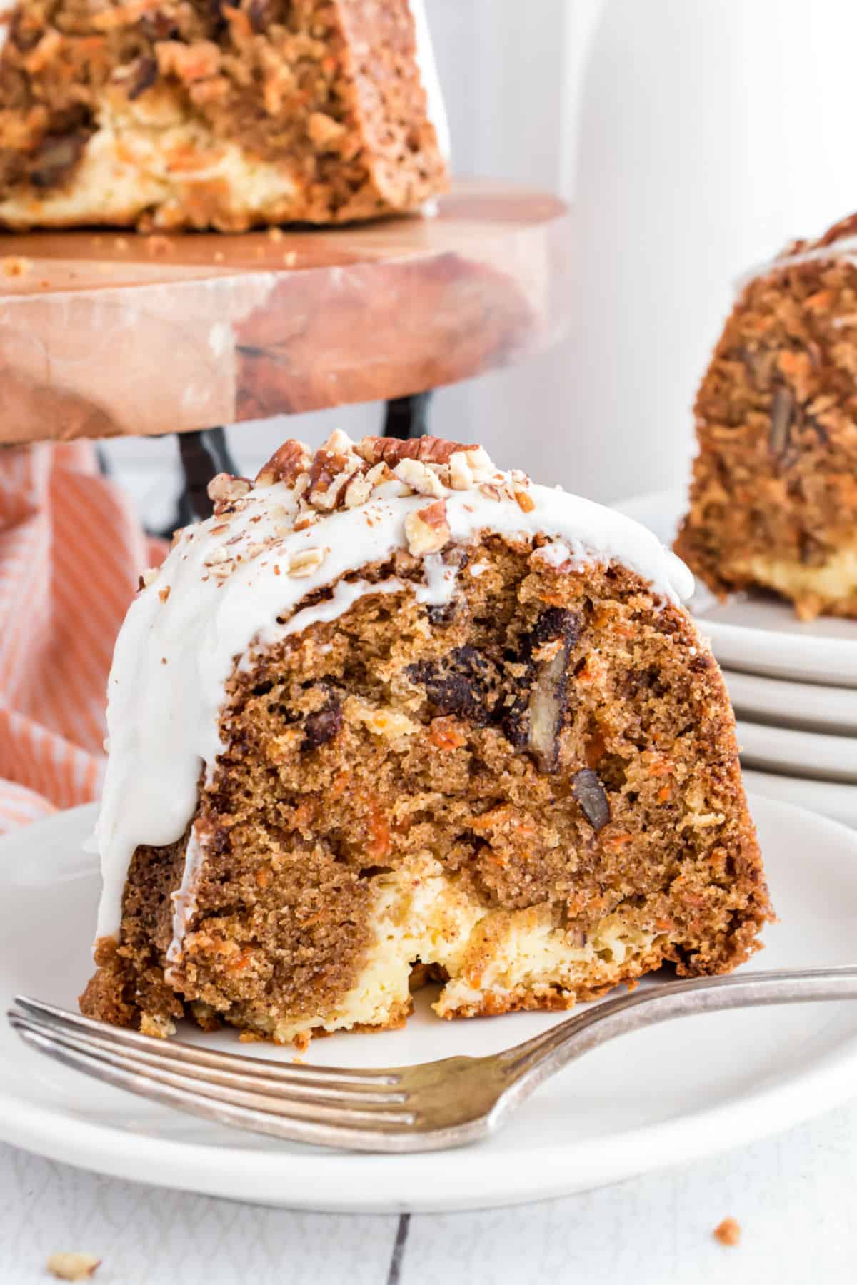 Slice of carrot bundt cake on a plate with cheesecake filling and frosting.