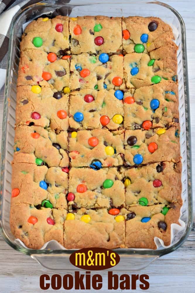 M&M chocolate chip cookie bars in a parchment paper lined 13x9 dish, cut into bars.