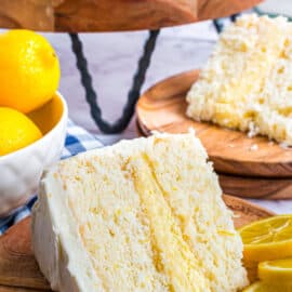 Slice of lemon layer cake with lemon curd filling on a wooden plate.
